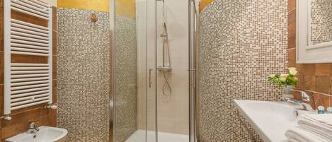 Un baño con ducha de vidrio, lavamanos blanco y bidé.