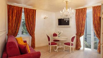 A room with a red sofa, a dining table with chairs, a chandelier, and large windows with patterned curtains.