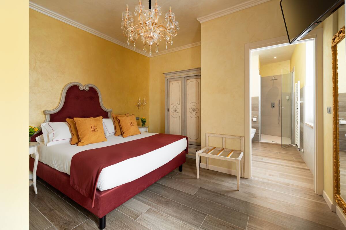 A bedroom with a large bed, a chandelier, a bedside table, and a wardrobe.