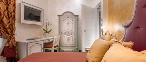 A bedroom with a bed, a desk, a chair, a wardrobe, and a television.