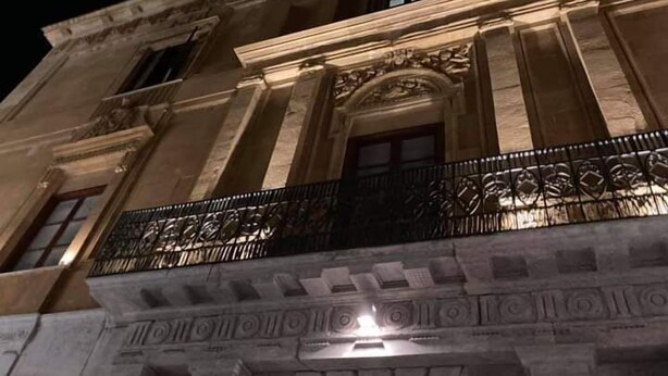 A historic building with classical architecture, featuring a balcony with ornate metal railings and a stone facade.
