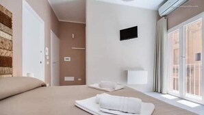 A hotel room with a large bed, a flat-screen TV mounted on the wall, and a window with a view of the outside.