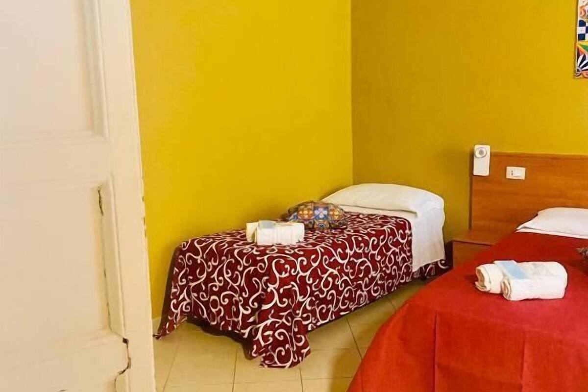 Ein kleines Hotelzimmer mit zwei Betten, eines mit einem gemusterten Überwurf und das andere mit einem einfarbigen Überwurf.