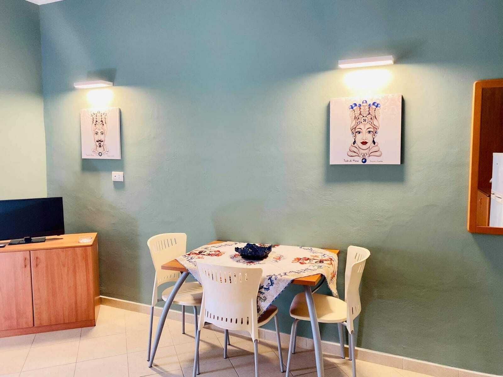 A dining area with a table set for two, two chairs, a wooden cabinet, and two wall-mounted light fixtures.