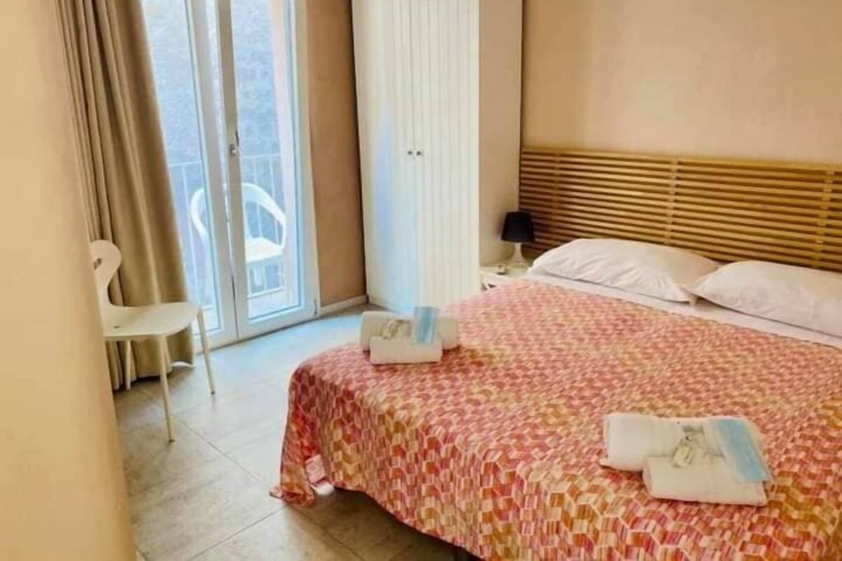 Ein Hotelzimmer mit Bett, Sessel, Nachttisch und einem Fenster mit Vorhängen.