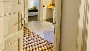A hallway with a patterned floor leading to a bedroom with a bed and a nightstand.