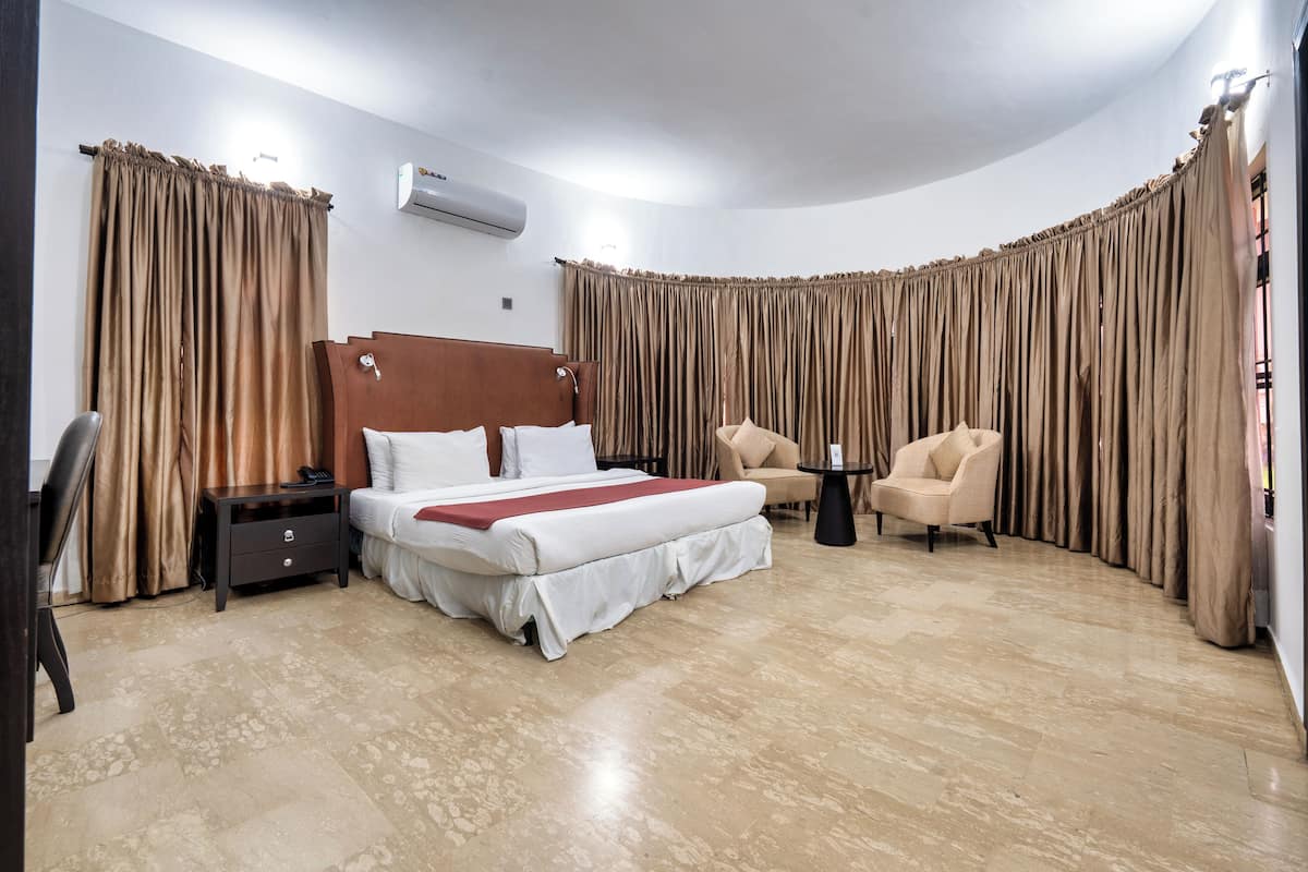 Ein Hotelzimmer mit Bett, Stuhl, kleinem Tisch und Vorhängen.