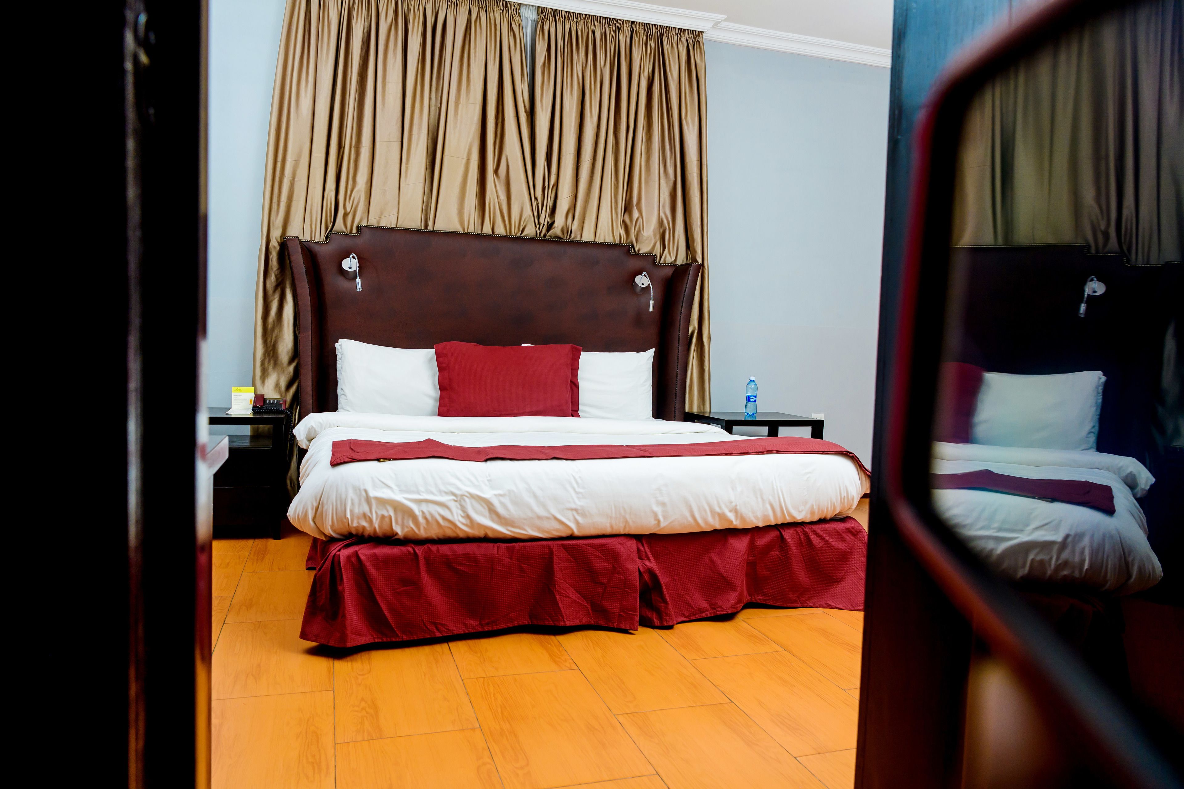 A hotel room with a large bed, a wooden floor, a nightstand, and a window with curtains.