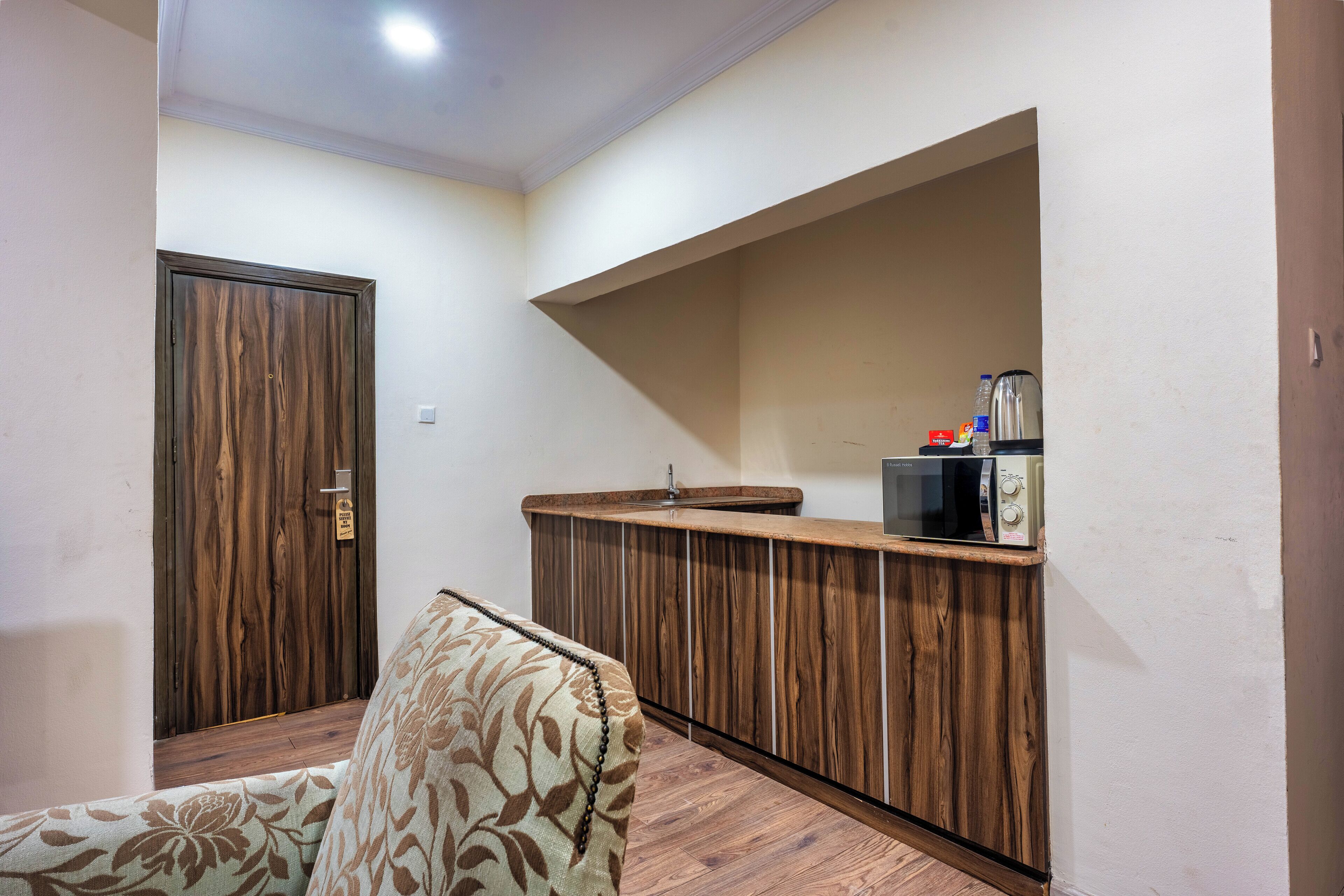 Una habitación con un armario de madera, un sofá estampado con motivos florales y un estante empotrado para microondas.