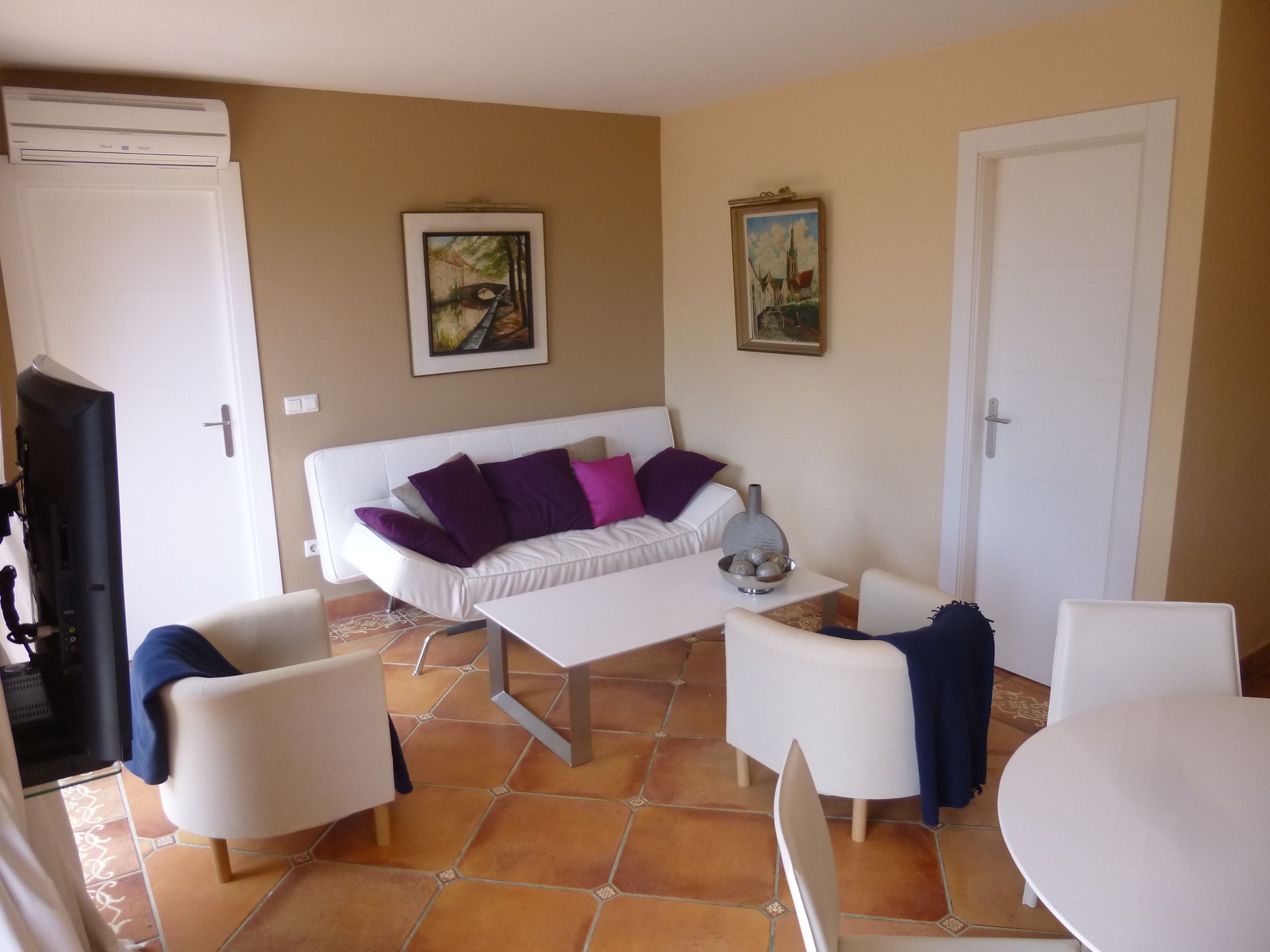 A living room with a white sofa, two white armchairs, a coffee table, and a TV.