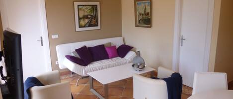 A living room with a white sofa, two white armchairs, a coffee table, and a TV.