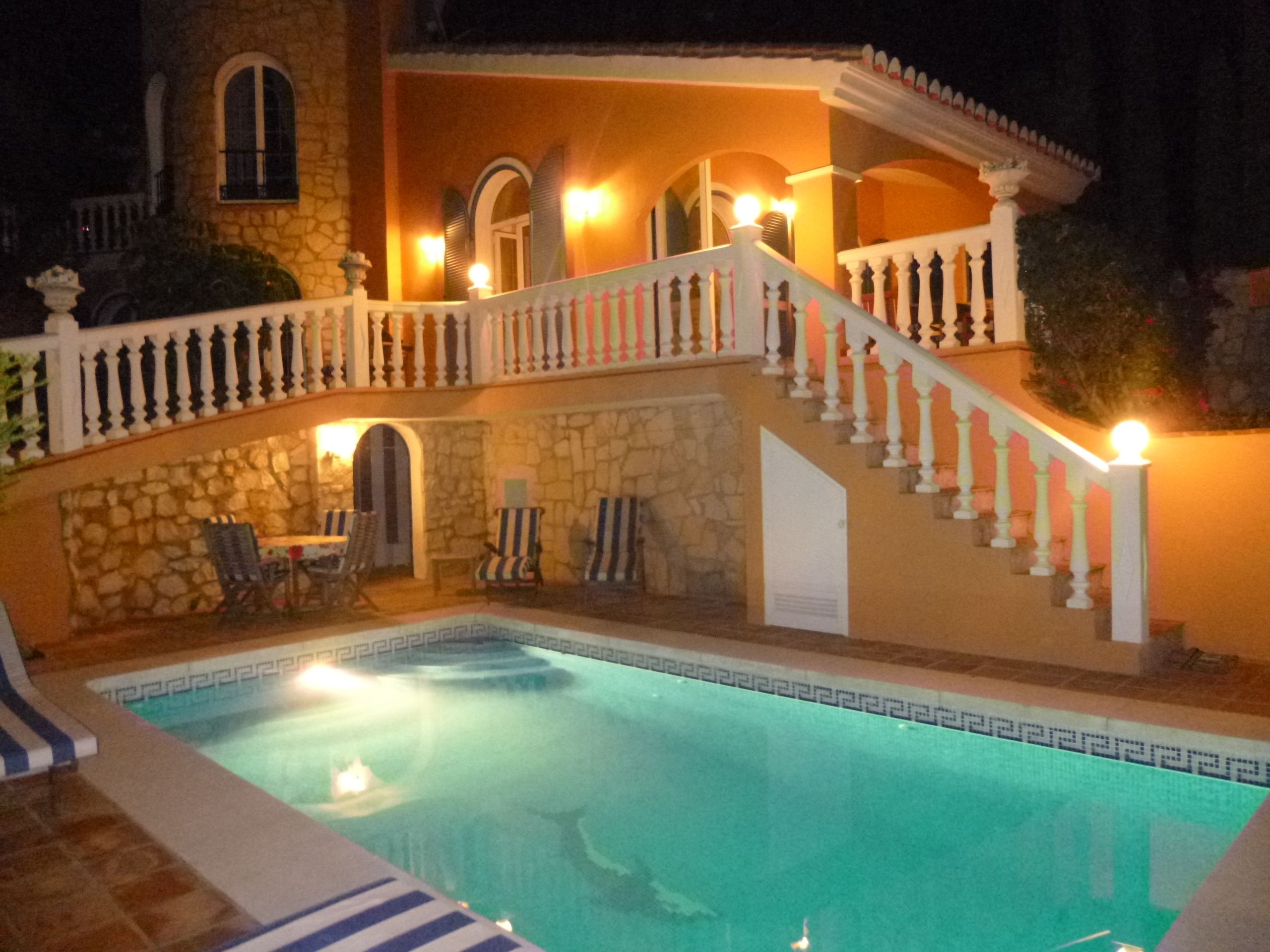 A pool area with a stone wall, a staircase with white balustrades, and outdoor seating.