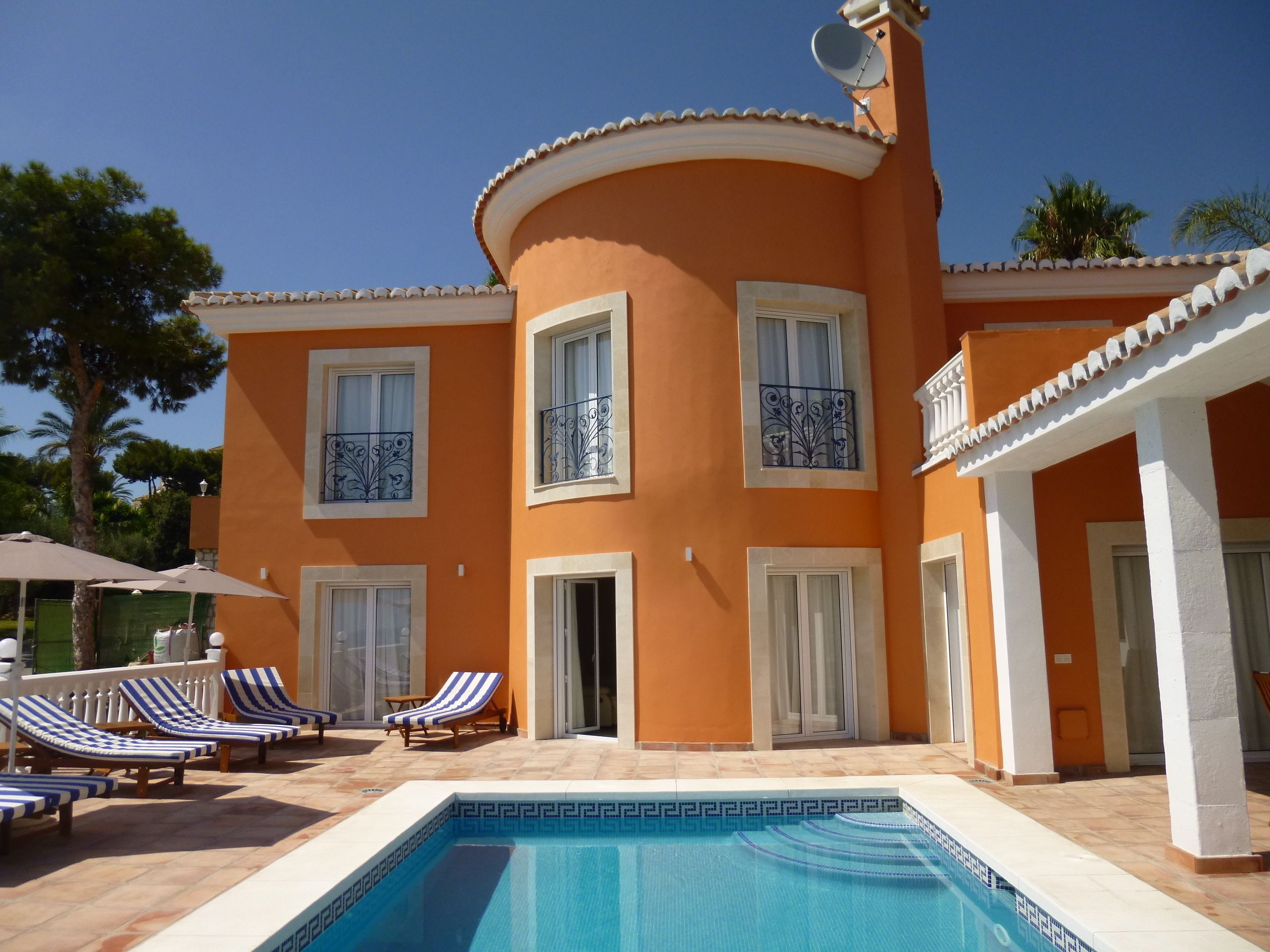 A two-story building with a swimming pool, lounge chairs, and a covered patio area.