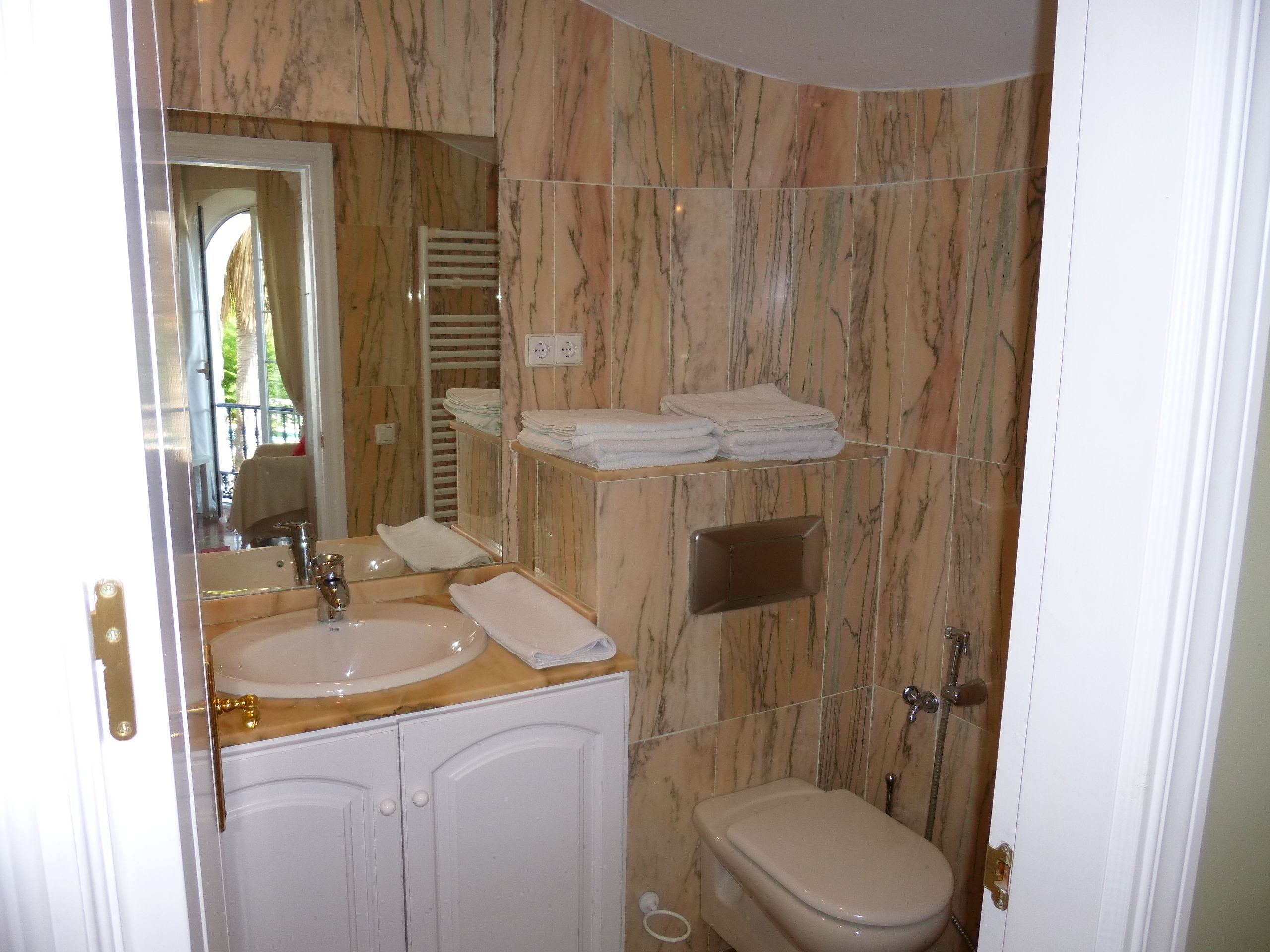 A bathroom with marble walls, a sink, a toilet, and a towel rack.