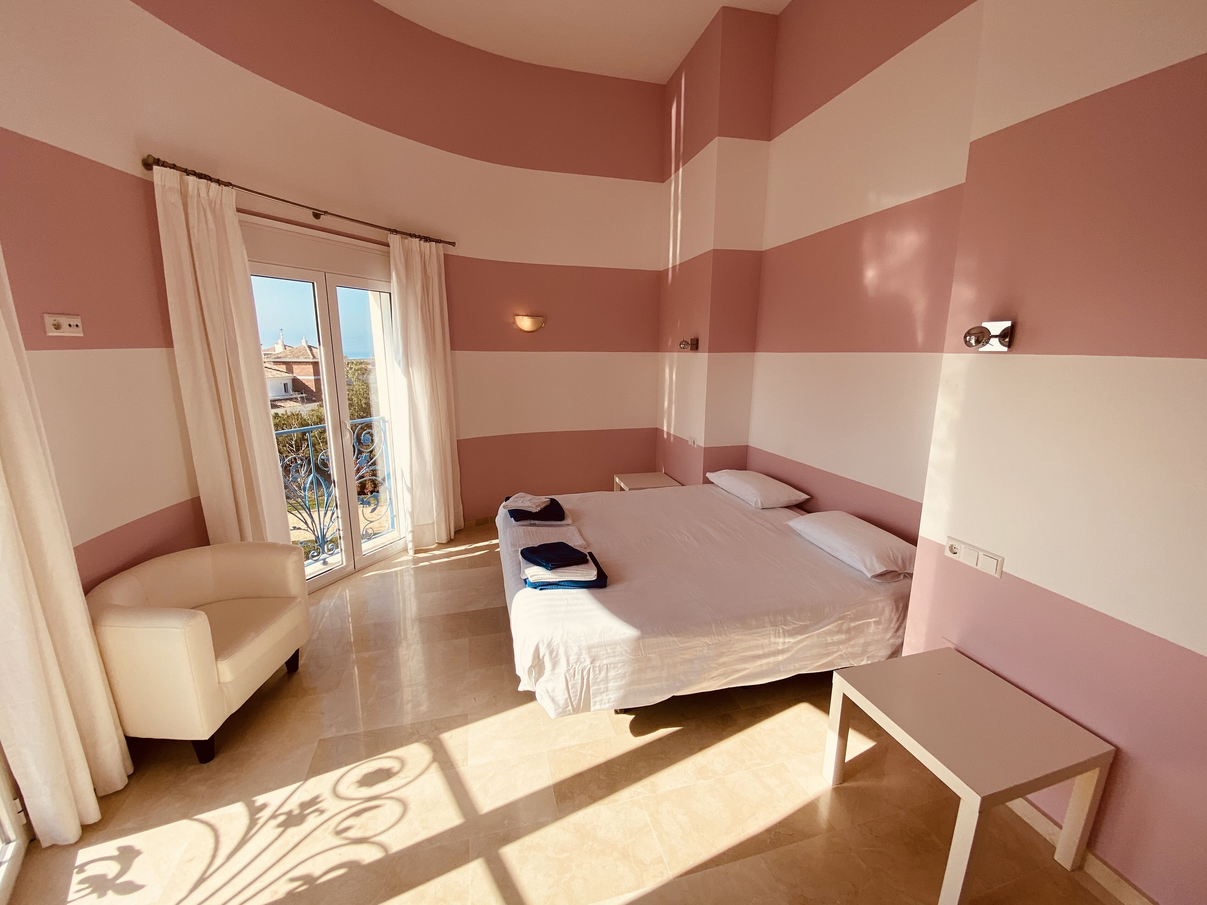 A bedroom with a bed, a chair, a small table, and a view through a glass door.