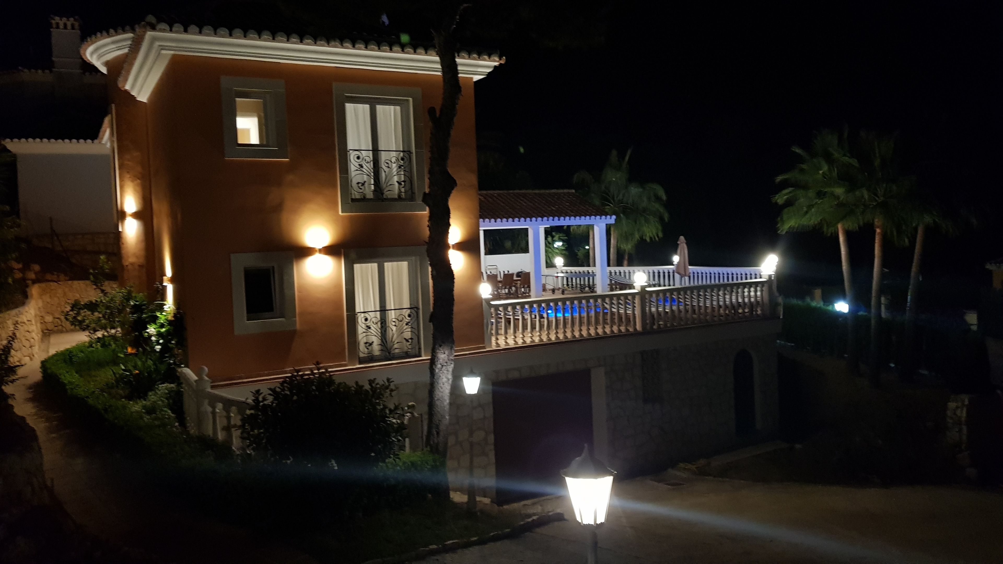 A two-story building with a balcony, a stone bridge, and a well-lit entrance.