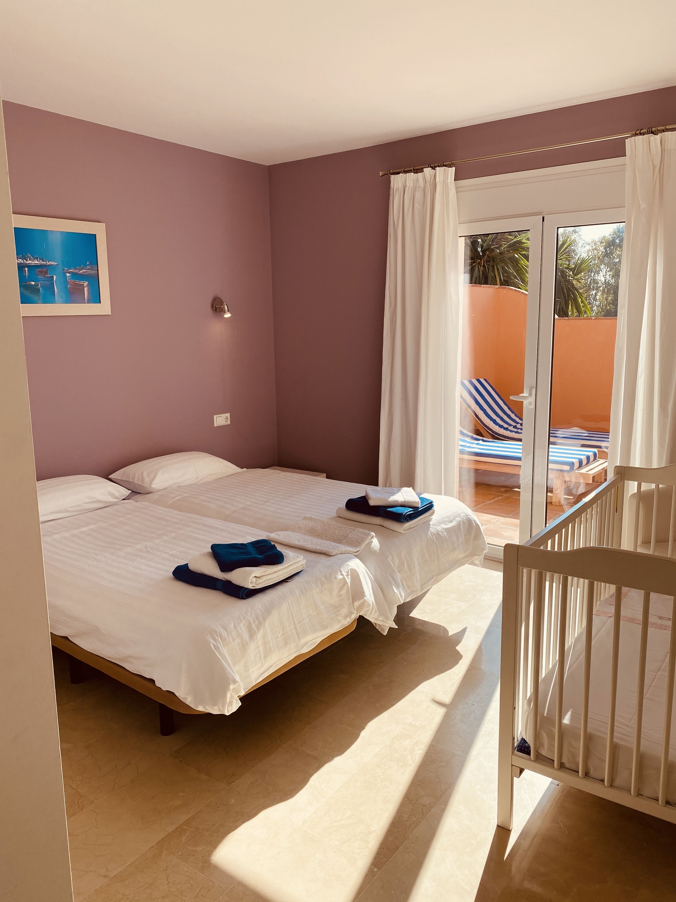 A bedroom with two beds, a view of the outside, and a small balcony area.