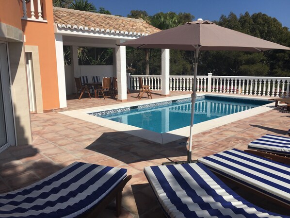 A swimming pool with lounge chairs and an umbrella, surrounded by a tiled patio and a white fence. - La Perla de Torrenueva (Mijas)