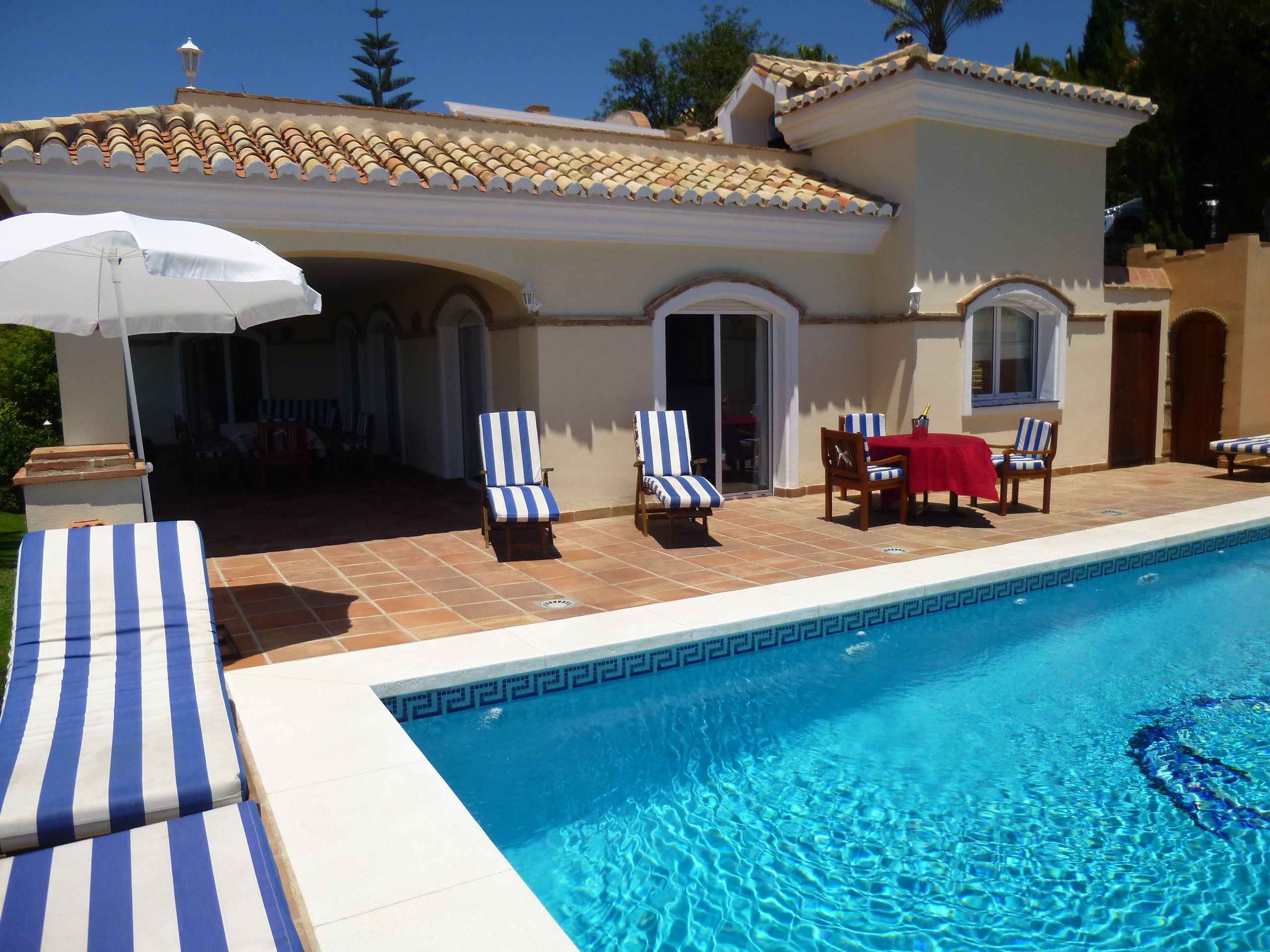 A swimming pool with lounge chairs and a table, surrounded by a tiled patio area.