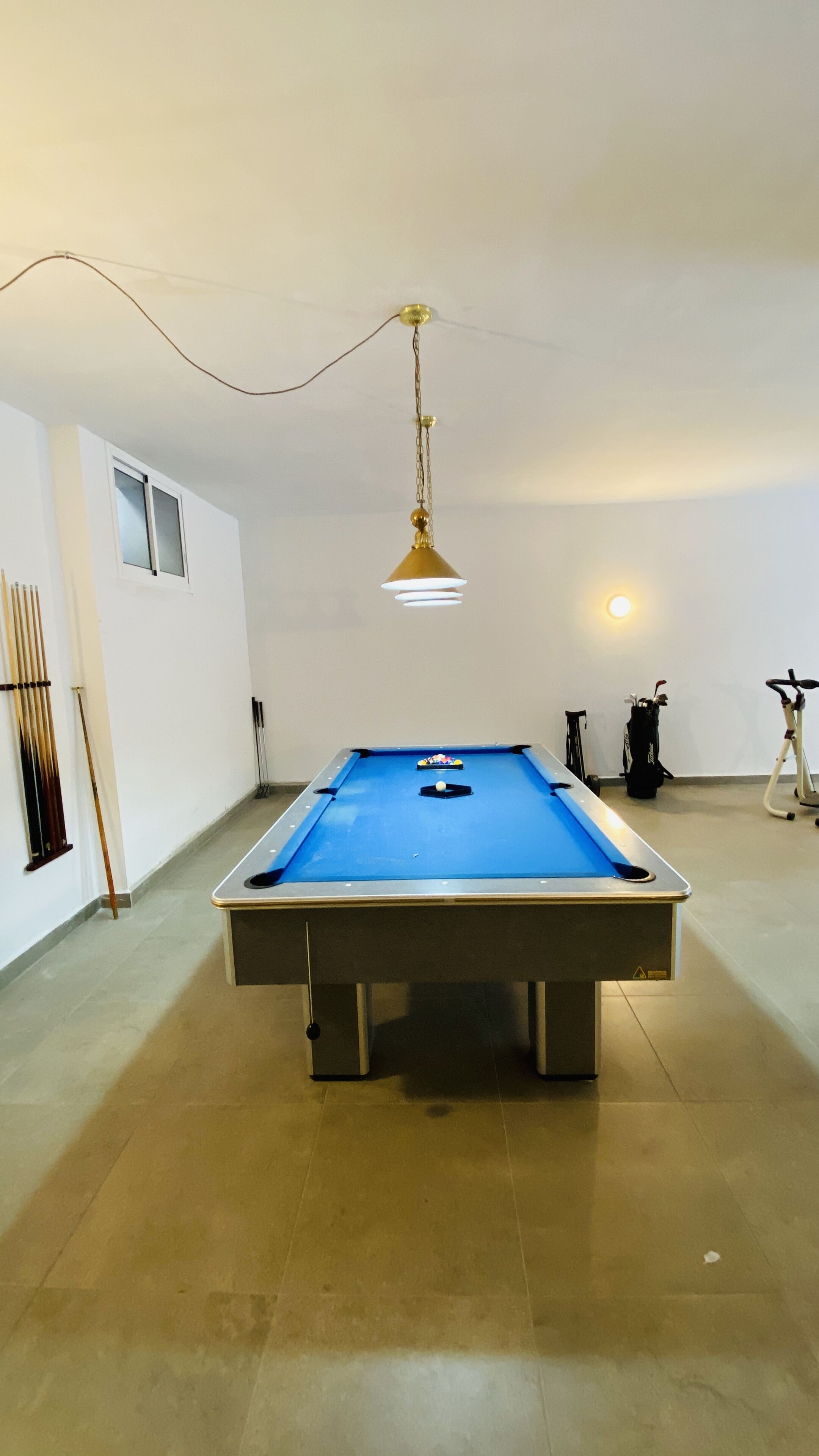 Une table de billard avec un luminaire suspendu, une fenêtre et un porte-ques fixé au mur.