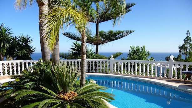 A swimming pool with a white fence, surrounded by palm trees and a view of the ocean. - La Perla de Torrenueva (Mijas)