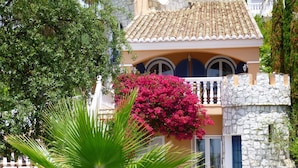 A Mediterranean-style building with a stone facade, a balcony with blue shutters, and a vibrant pink bougainvillea. - La Perla de Torrenueva (Mijas)