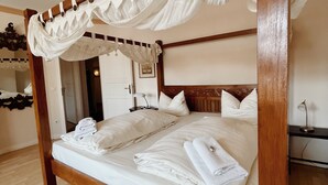 Ein Bett mit Baldachin, ausgestattet mit weißen Leinen und Handtüchern, ein hölzerner Kopfteil und ein Holzboden.