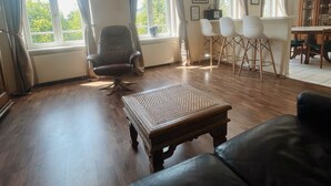 Ein großzügiger Wohnraum mit großem Fenster, einem Holztisch, einer Ledersofa und einem Essbereich mit Stühlen.