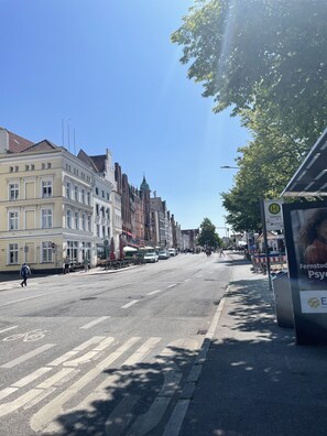 Eine Straße mit historischen Gebäuden, einer Straßenbahnhaltestelle und einer Bushaltestelle mit Werbung für Fernstudium.