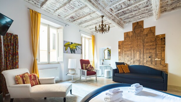A hotel room with a bed, a sofa, a chair, a desk, and artwork on the walls. - Babuccio Art Inn (Rome)