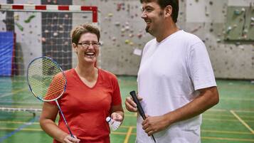 Deux personnes dans une salle d’escalade intérieure : l’une tient une raquette de badminton et l’autre, une raquette de tennis.