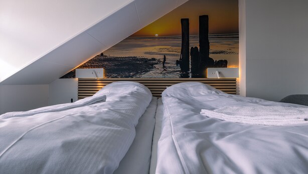A bedroom with two beds, a view of the sunset over the ocean, and a modern design with a sloped ceiling.