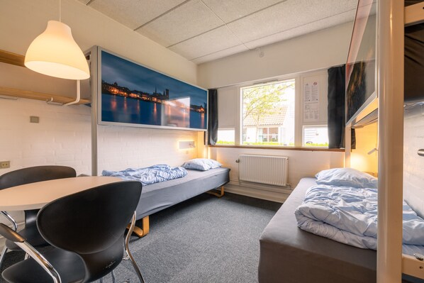 A dormitory room with a single bed, a desk, and a chair. There is a window with a view of a cityscape at night. - Danhostel Ribe (Ribe)