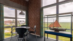 A room with a brick wall, large windows, a table with chairs, and a model ship on display.