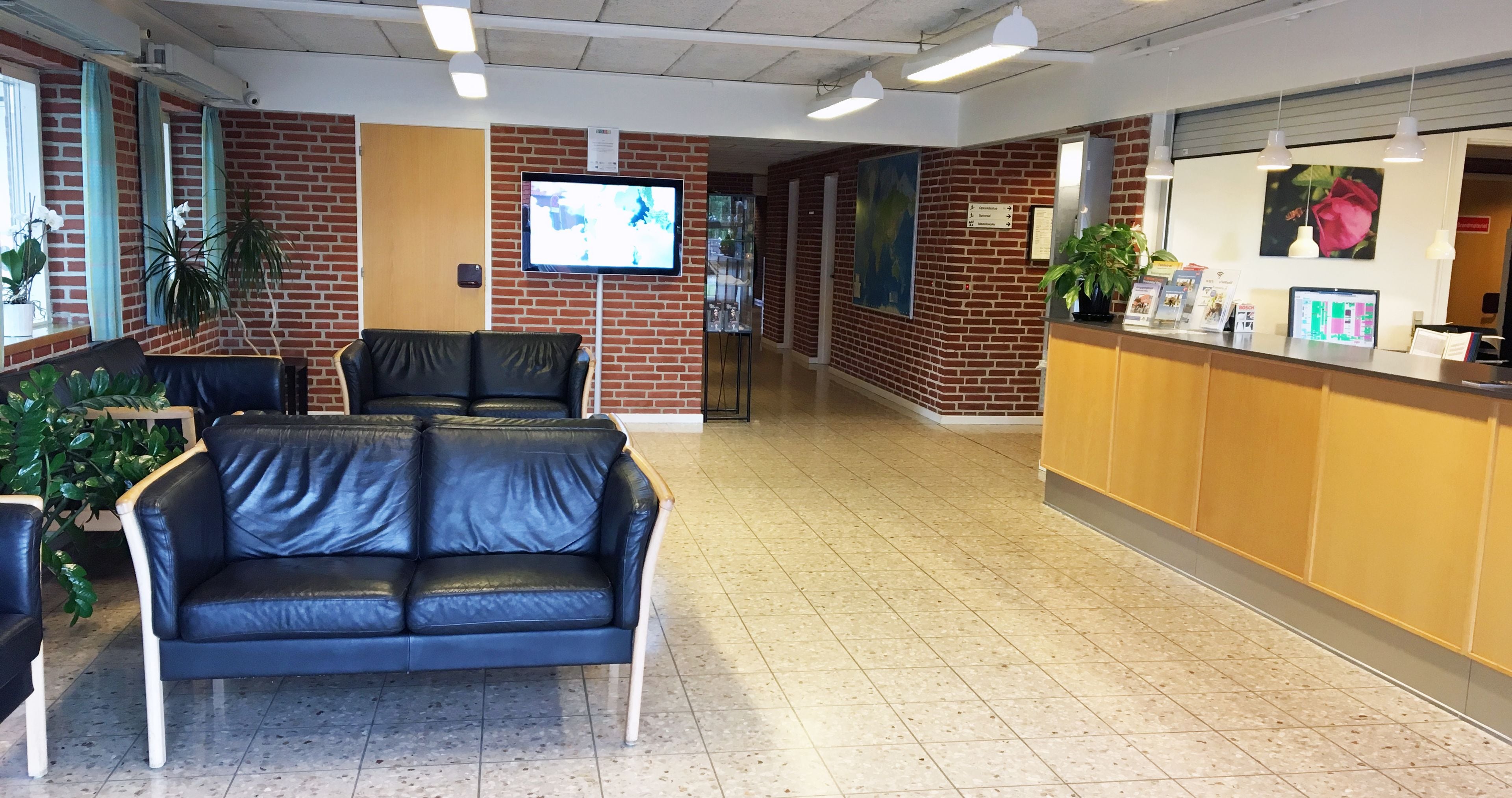 A reception area with a brick wall, a black leather couch, a reception desk, and a television screen.