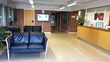 A reception area with a brick wall, a black leather couch, a reception desk, and a television screen.
