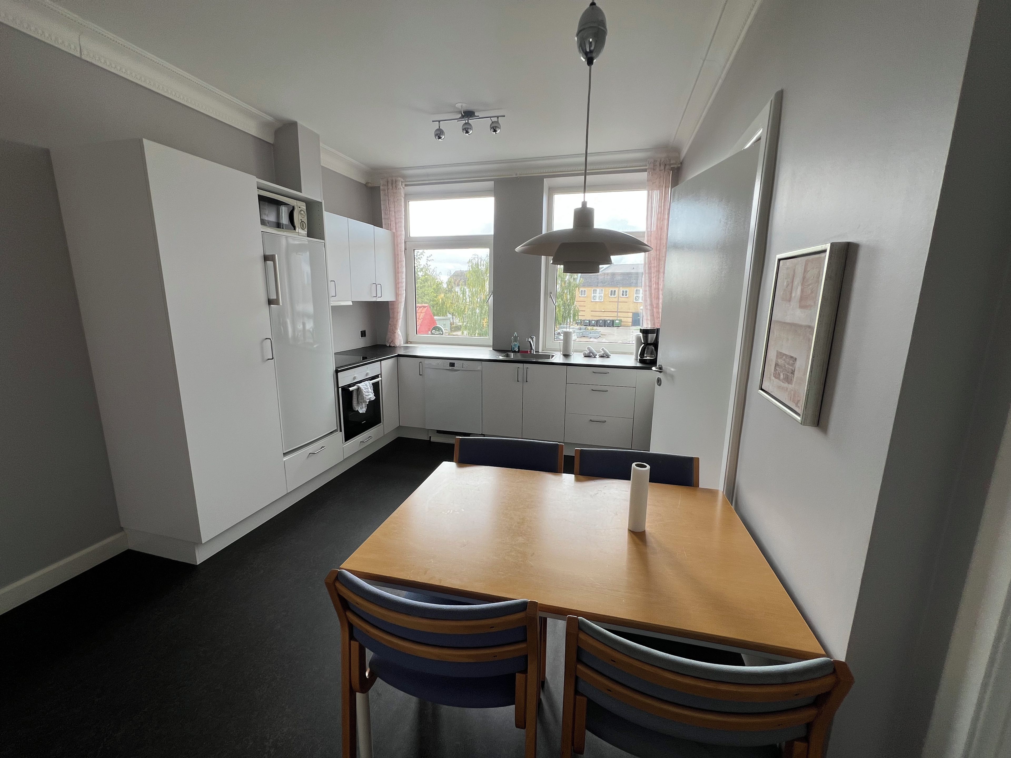 A modern kitchen with white cabinets, a wooden dining table, and a window with a view of the outside.