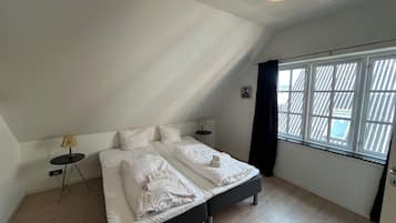 A bedroom with a bed, two bedside tables, a lamp, a window with curtains, and a ceiling light.