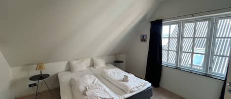 Un dormitorio con una cama, dos mesitas de noche, una lámpara, una ventana con cortinas y una luz en el techo.