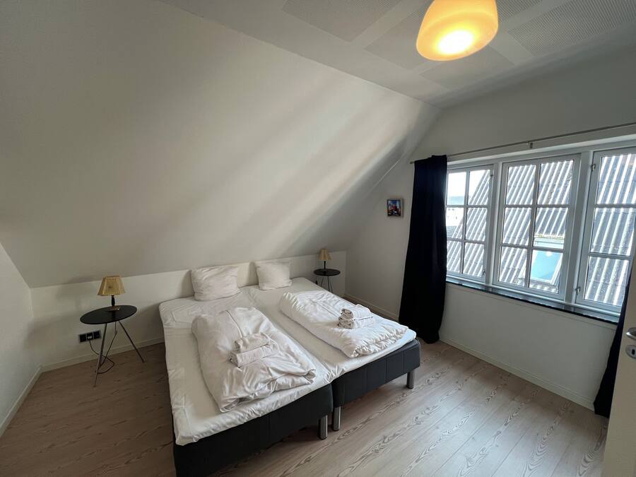 A bedroom with a bed, two bedside tables, a lamp, a window with curtains, and a ceiling light.