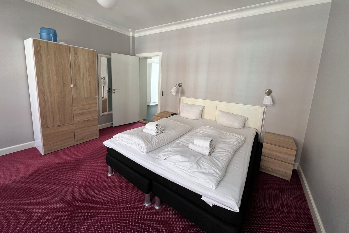 A hotel room with a large bed, a wardrobe, a mirror, and a bedside lamp.