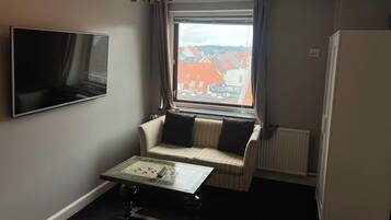 Hotelkamer met televisie, een klein tafeltje, een bank, een raam met uitzicht op gebouwen en een radiator.