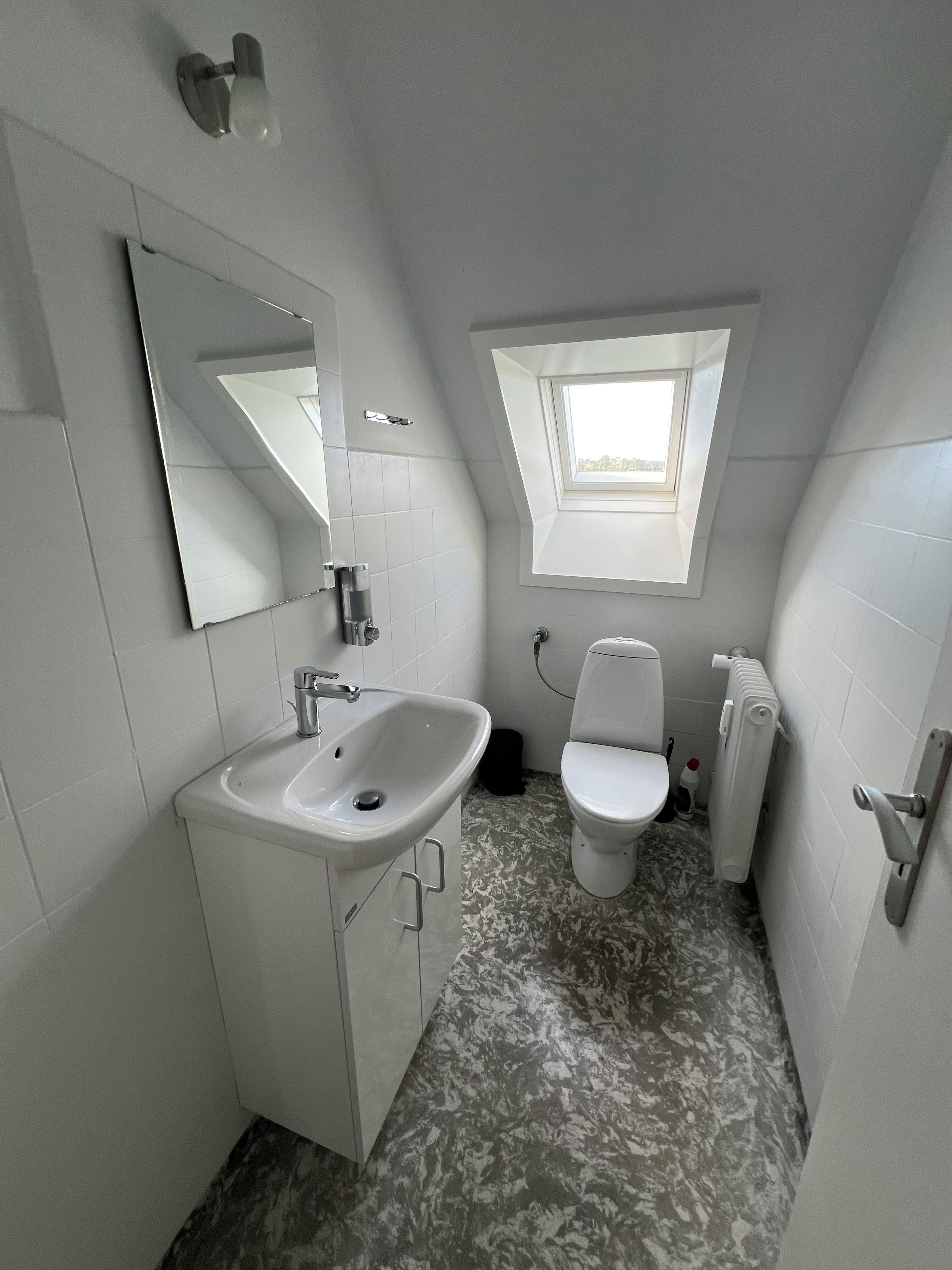 Un baño con lavamanos blanco, inodoro y tragaluz.