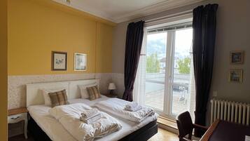 A hotel room with a large bed, a dining table, a chandelier, and a view of the outdoors.