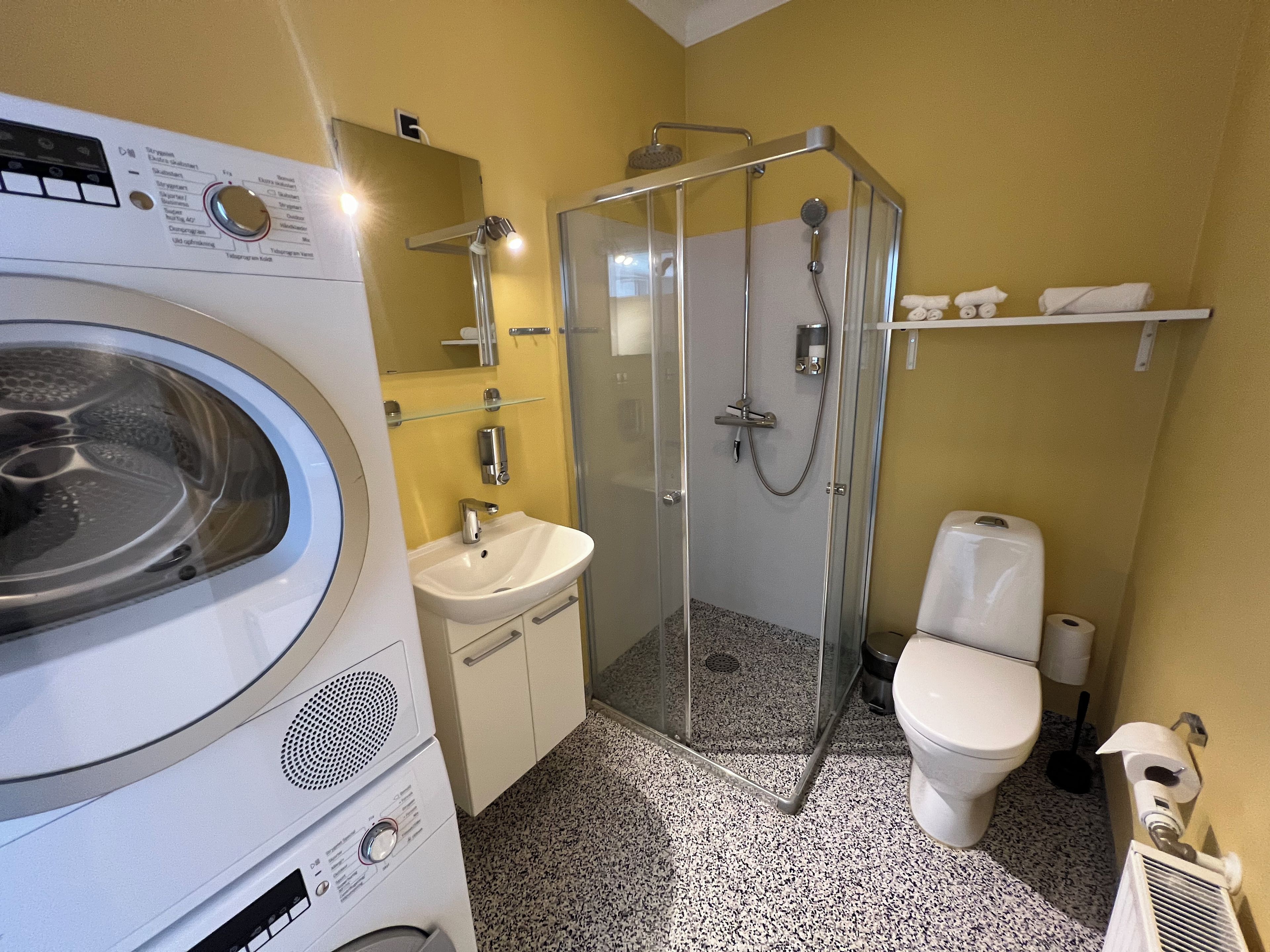 Un baño pequeño con lavadora, lavamanos, inodoro y cabina de ducha con paredes de vidrio.
