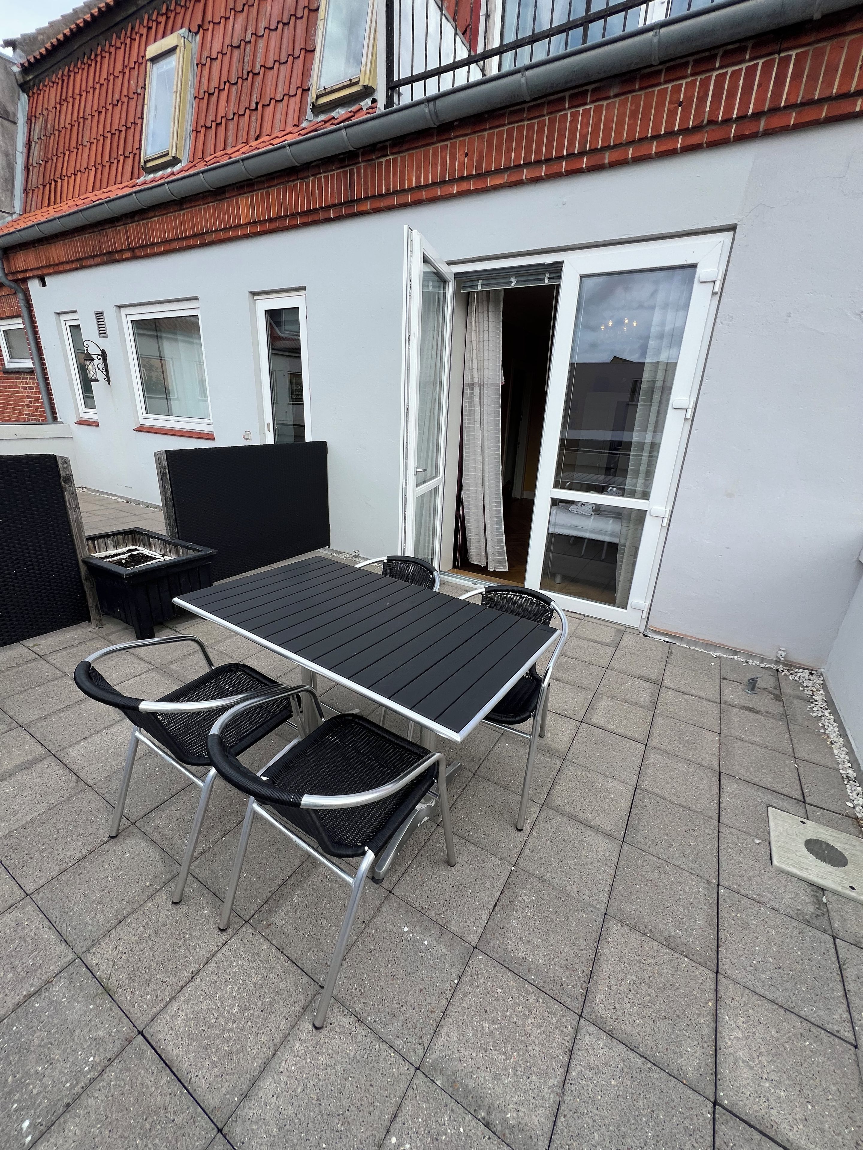En udendørs terrasse med et bord og stole, en skydedør og en murstensv æg.