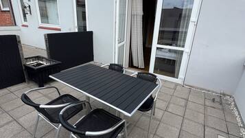 En udendørs terrasse med et bord og stole, en skydedør og en murstensvæg.