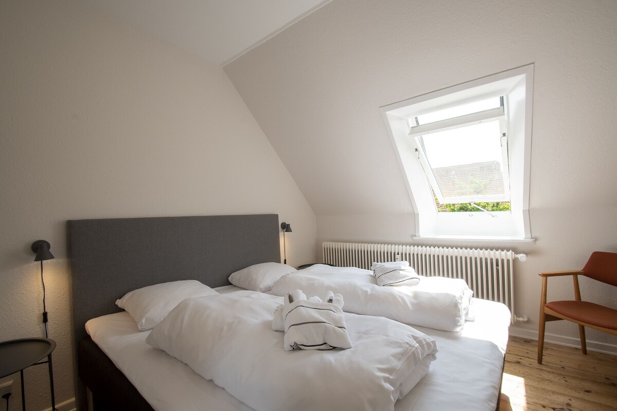 Una camera da letto con due letti, un termosifone, una finestra, una sedia e una lampada.