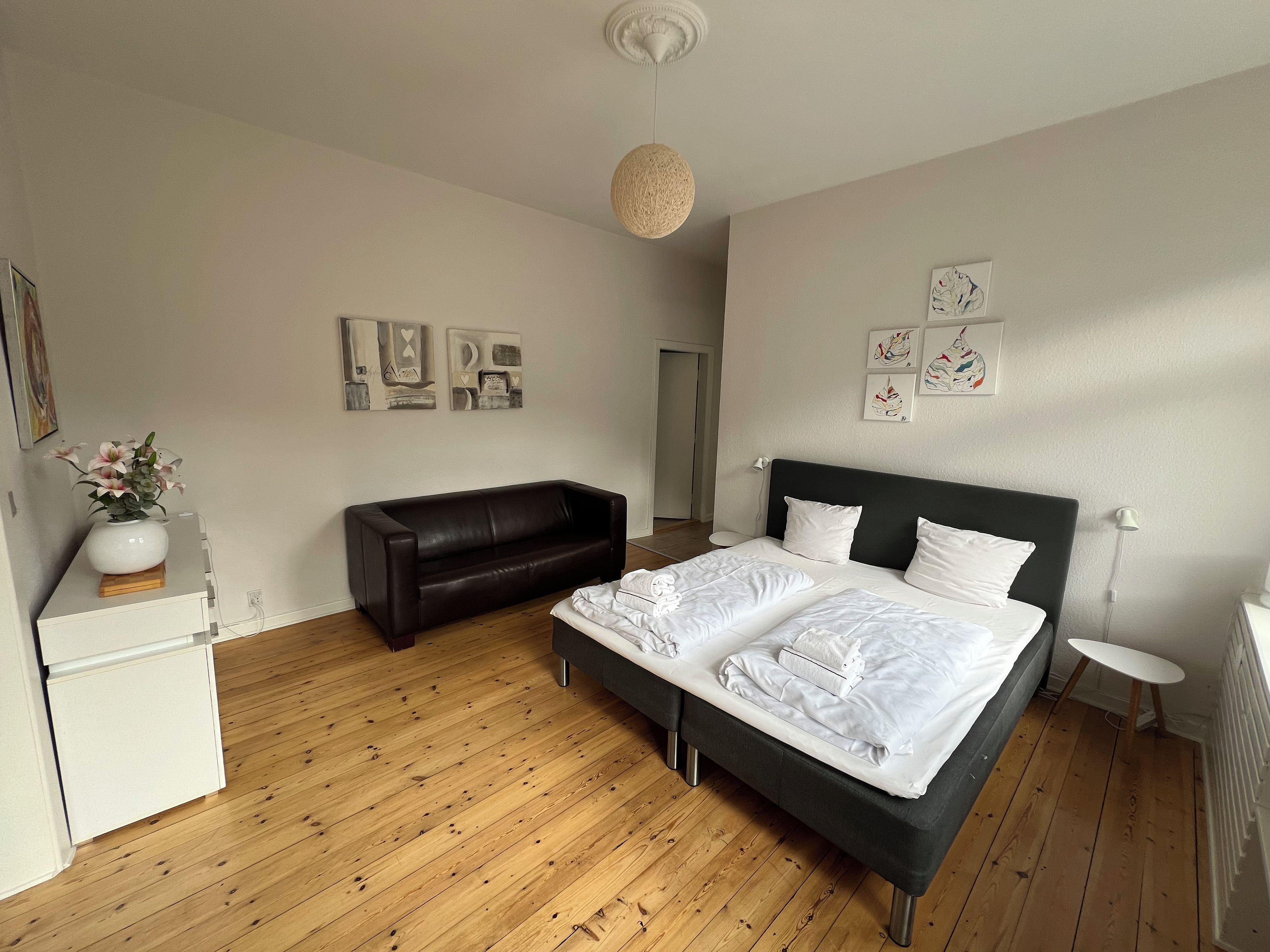 Ein Schlafzimmer mit einem Bett, einem Schlafsofa, einem kleinen Tisch und einer Wand mit Kunstwerken.