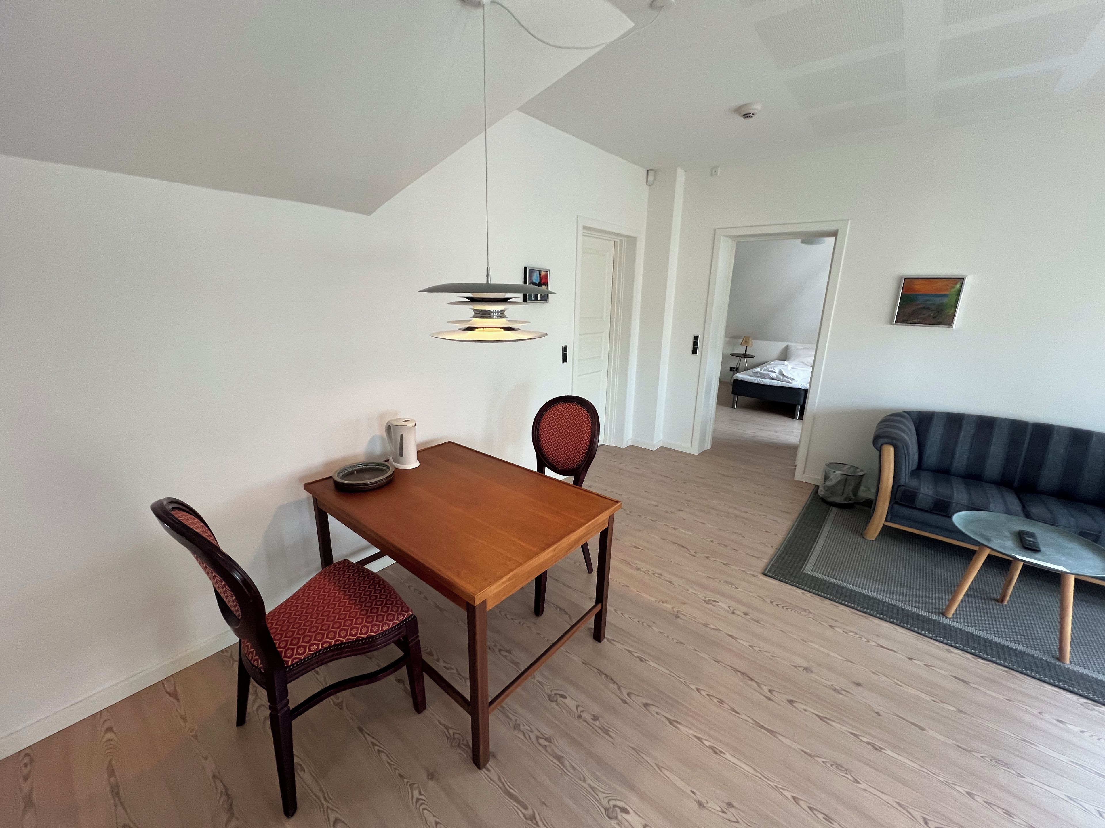 A room with a dining table, two chairs, a sofa, a bed, and a painting on the wall.
